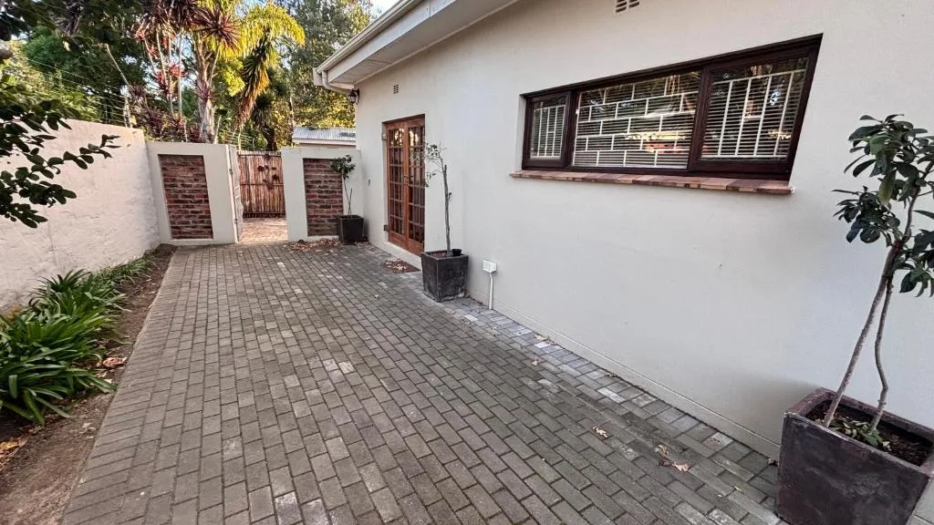 White cottage exterior with paved driveway, wooden doors, and tropical plants