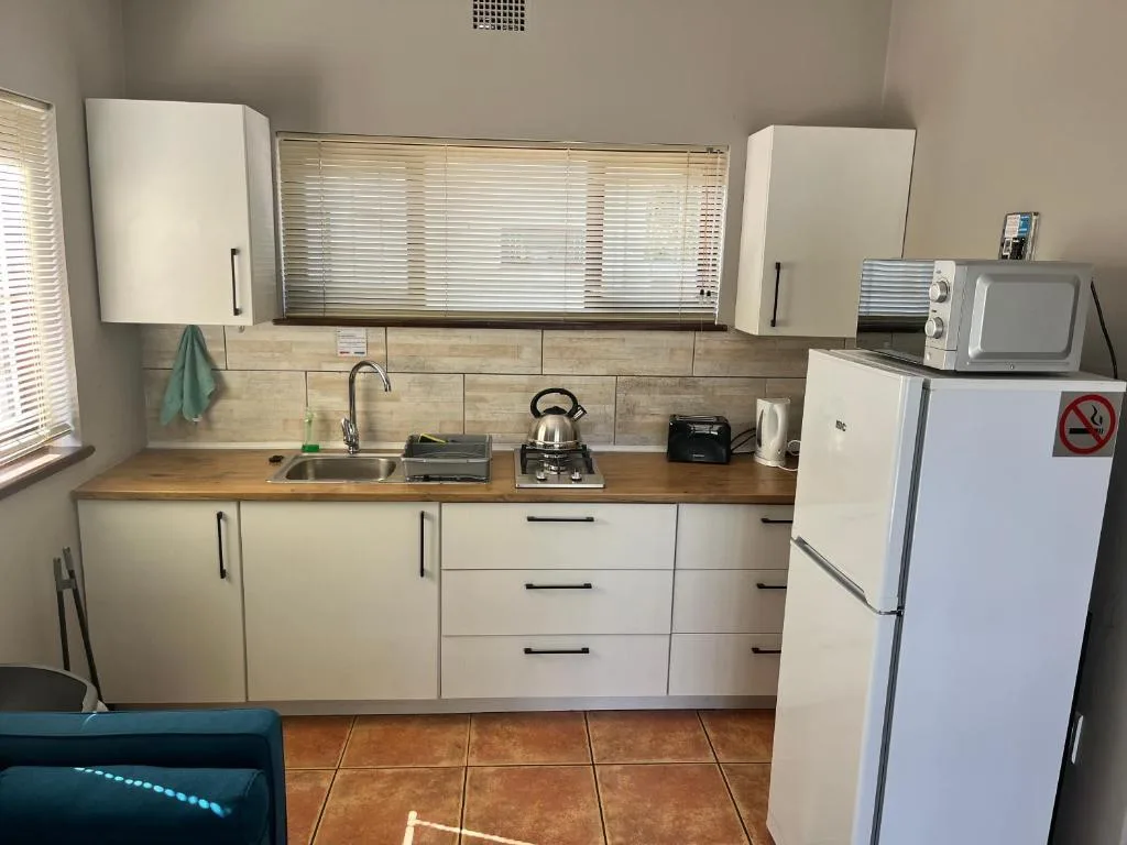 Compact kitchen with white cabinetry, wooden countertop, stainless steel sink, and refrigerator
