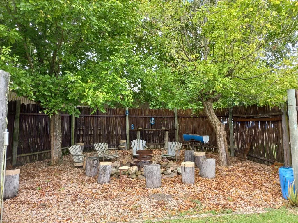 Outdoor fire pit area with Adirondack chairs and log seating surrounded by mature trees