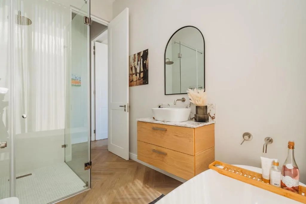 Modern bathroom with wooden vanity, round mirror, and walk-in shower enclosure