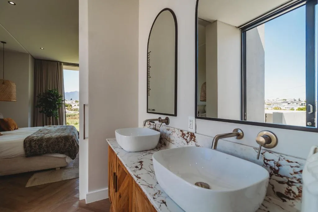 Modern bathroom with dual vessel sinks, marble countertop, and bedroom view beyond