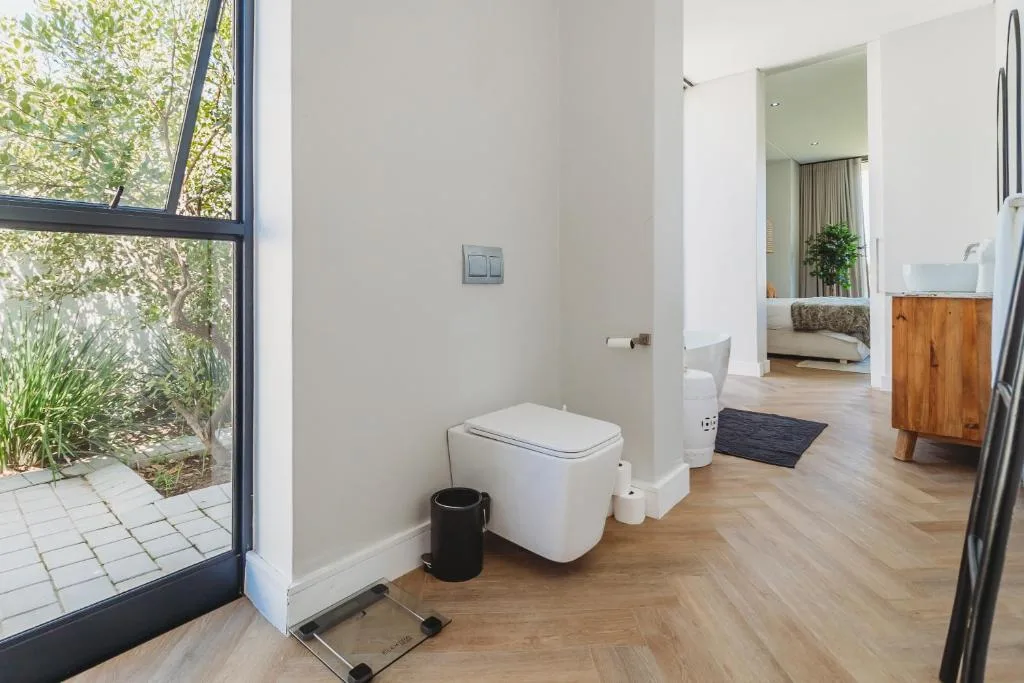 Modern bathroom with white toilet, wooden vanity, and garden view through large window