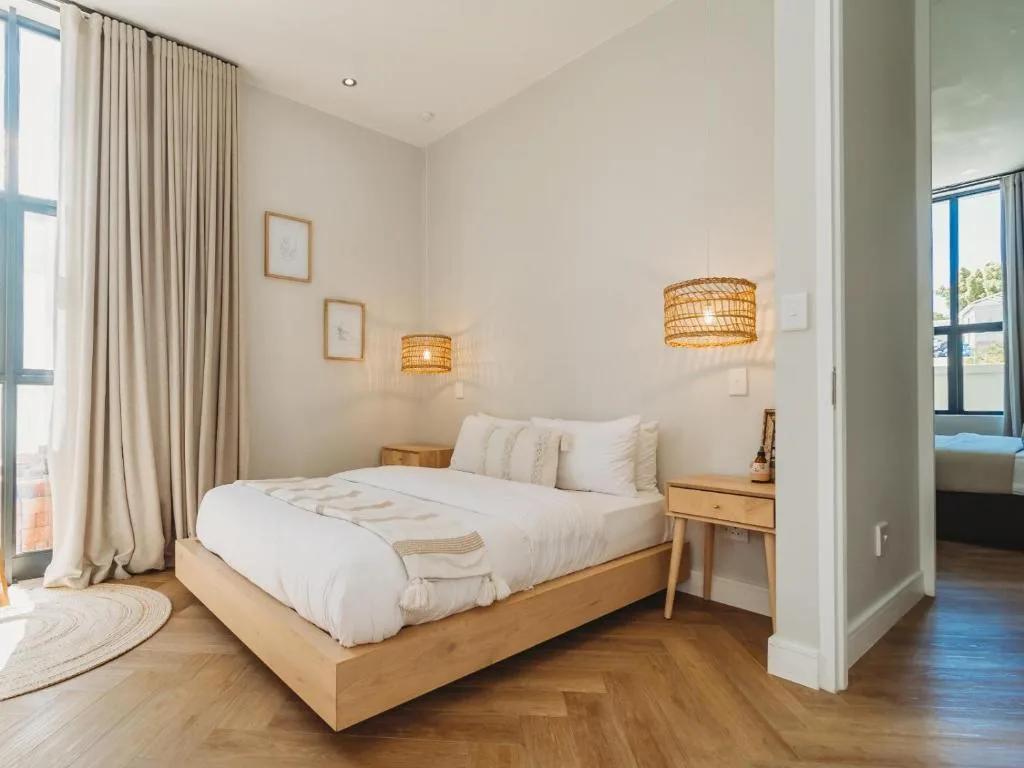 Bright bedroom with wooden bed, white linens, woven pendant lights, and curtains