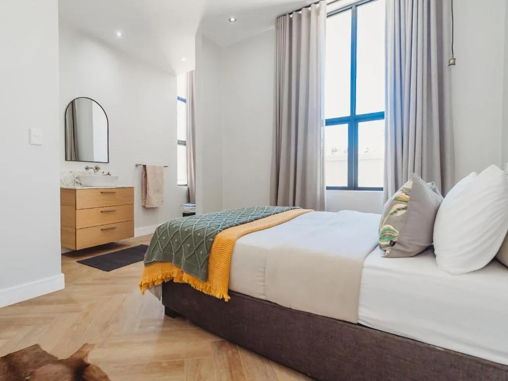 Bright bedroom with queen bed, wooden vanity, and large windows with blue frames