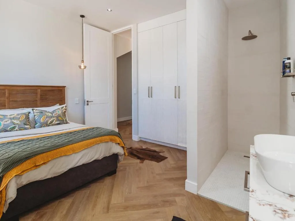 Modern bedroom with wooden bed frame, white wardrobes, and ensuite bathroom visible