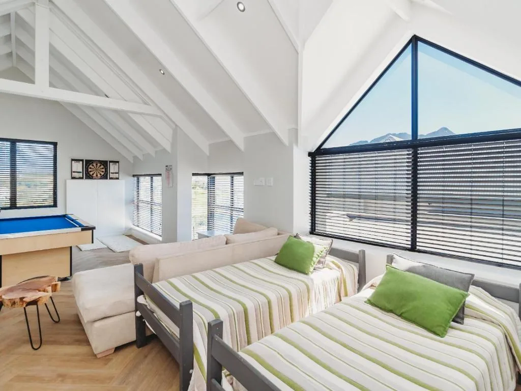 Bright bedroom with two beds, green pillows, and mountain views through large windows