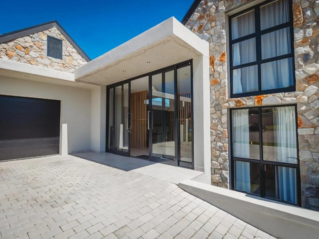 Modern villa entrance with stone facade, black-framed doors, and paved driveway