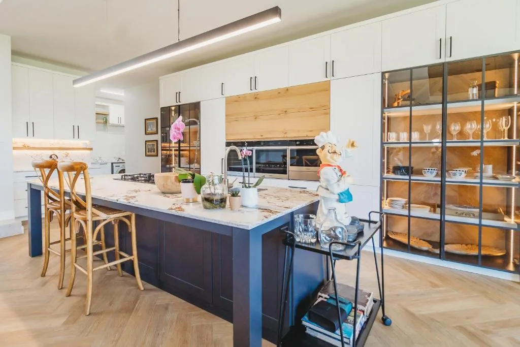 Modern kitchen with white cabinetry, dark island, and open shelving displaying glassware