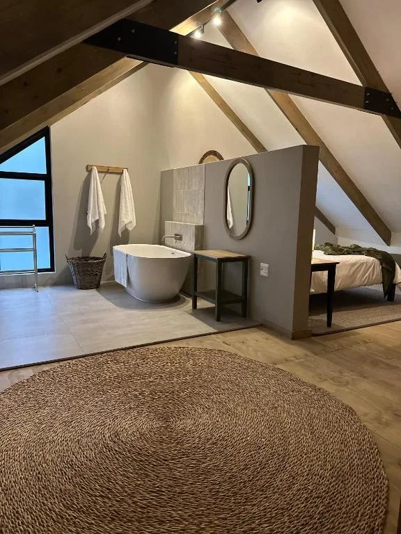 Modern bathroom with freestanding bathtub, round mirror, and vaulted ceiling beams