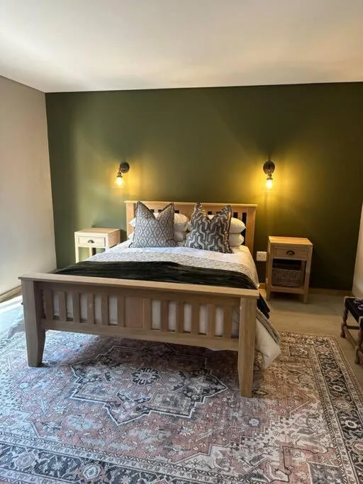 Spacious bedroom with wooden bed, olive green accent wall, warm lighting