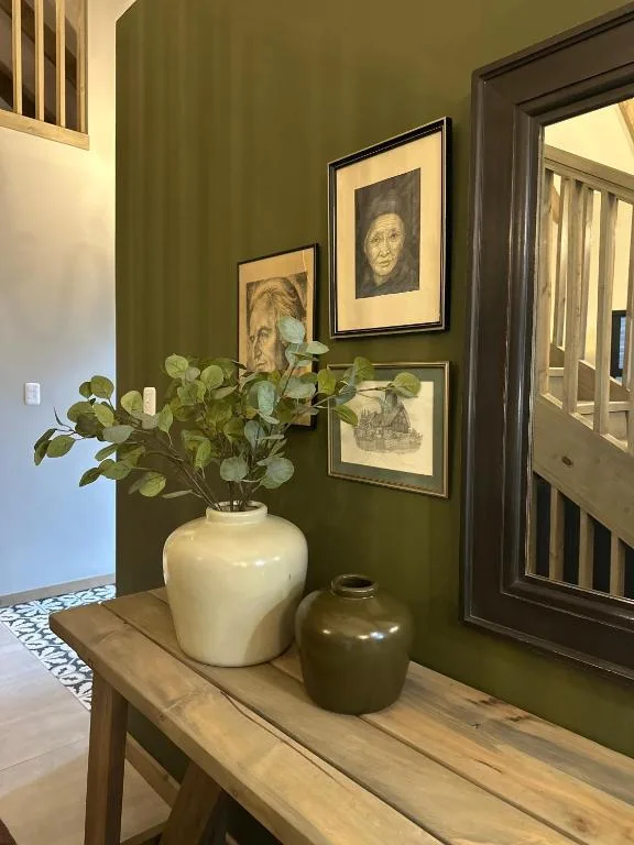Olive green hallway with framed portraits and white ceramic vase with greenery