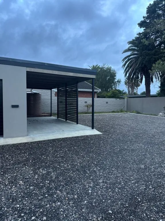 Modern white villa entrance with carport and gravel driveway, palm trees visible