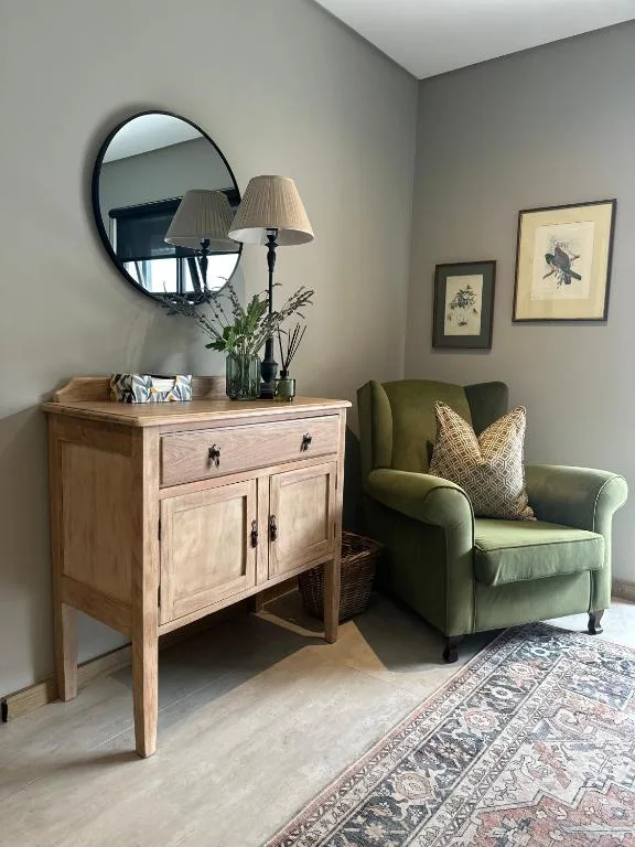 Cozy lounge corner with green armchair, wooden vanity, and round mirror