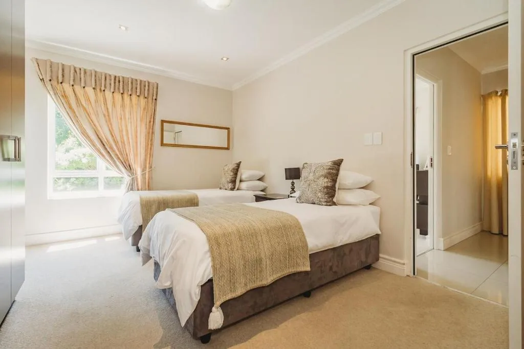 Twin beds with white linens and gold throws in bright, neutral bedroom