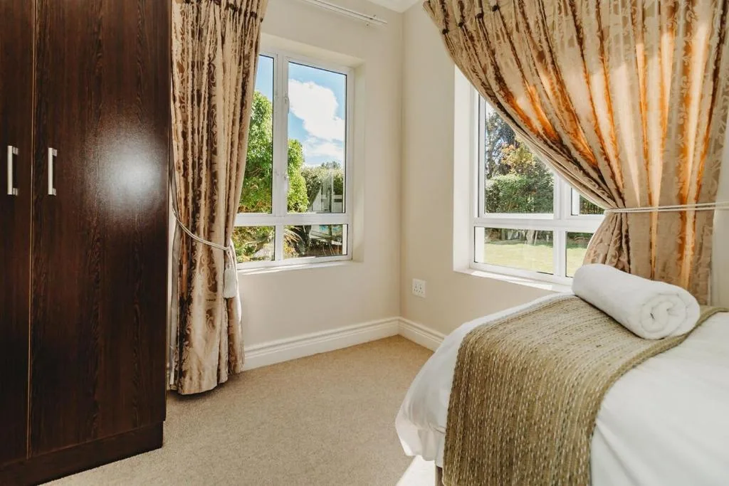 Bright bedroom with bed, dark wood wardrobe, garden views through large windows