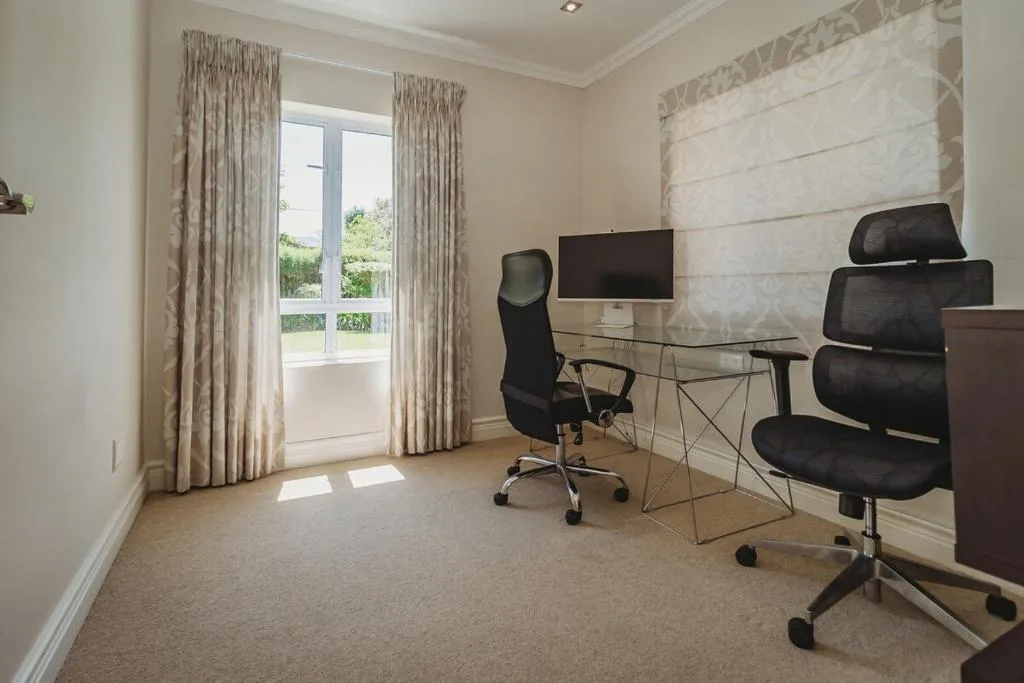 Modern home office with desk, ergonomic chairs, and garden views through doors