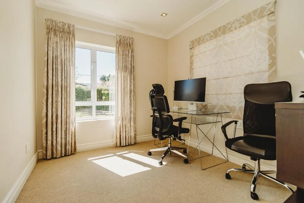 Modern home office with desk, ergonomic chairs, and garden views through windows