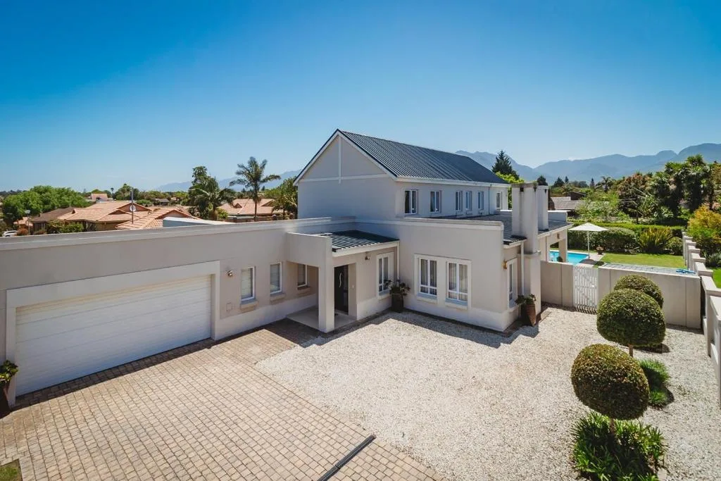 Modern white house with garage, driveway, and manicured gardens with mountain views