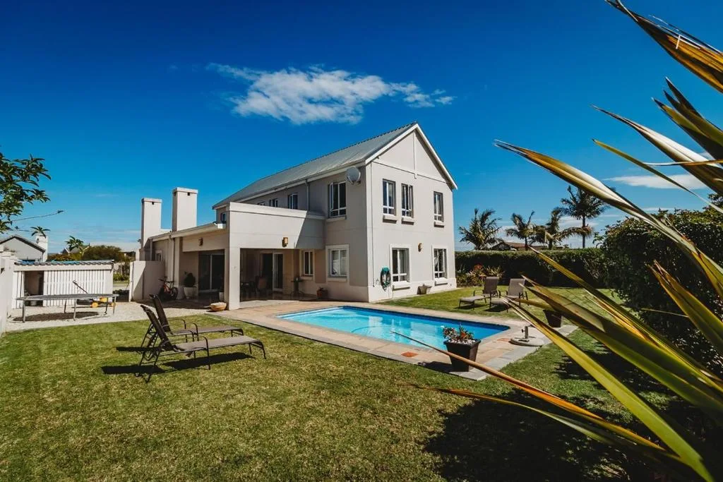 Modern white house with pool and manicured lawn under blue sky