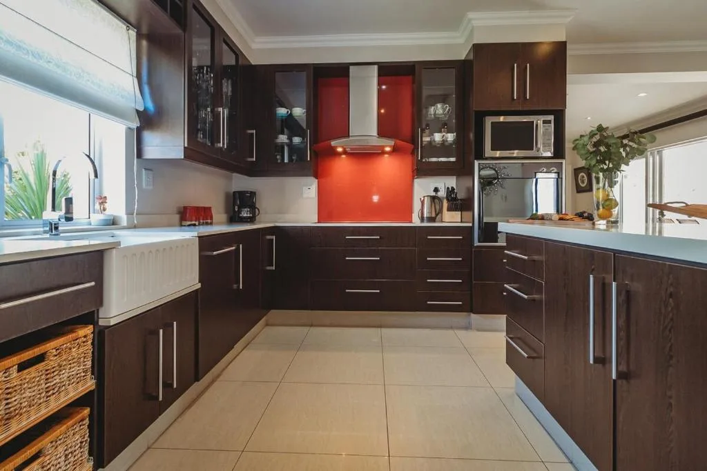 Modern kitchen with dark cabinetry, red backsplash, and stainless steel appliances