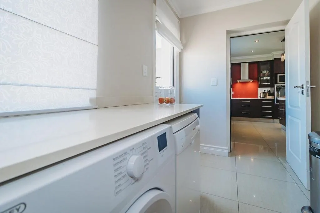 Modern kitchen with white counters, washing machine, and orange accents