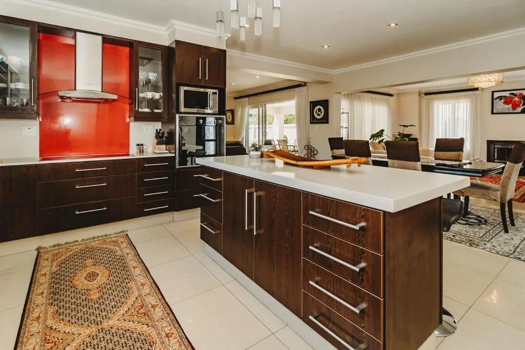 Modern kitchen with dark cabinetry, red splashback, and white island counter