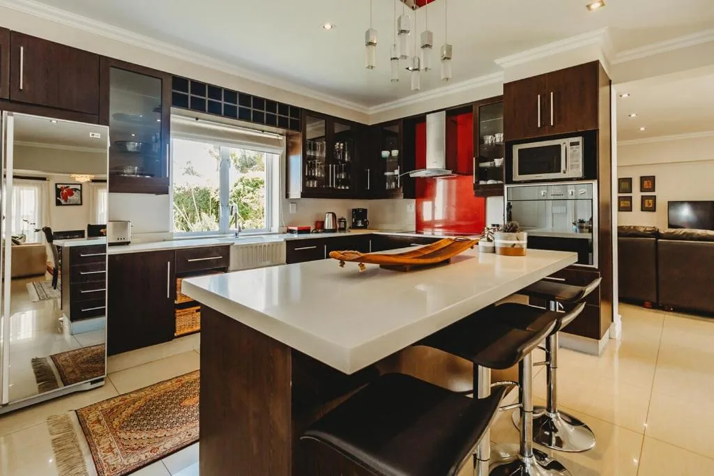Modern kitchen with dark cabinetry, white countertop island, and red backsplash