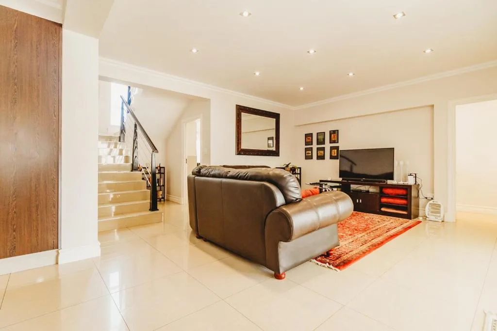Spacious lounge with brown leather sofa, TV, and cream tiled floors