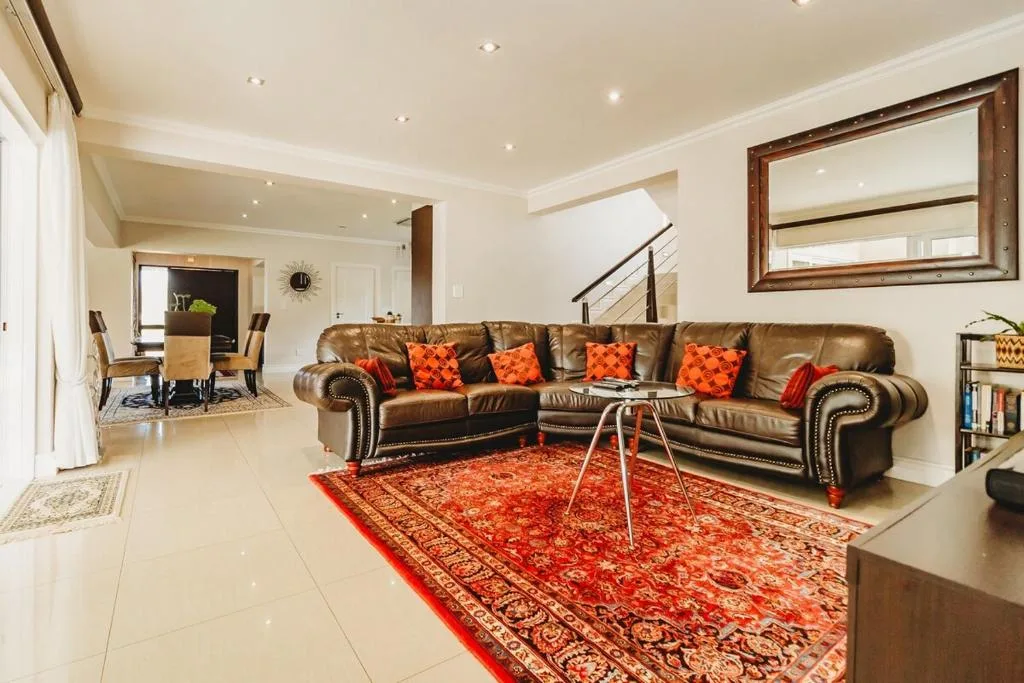 Spacious living room with brown leather sofa, orange cushions, and ornate red rug