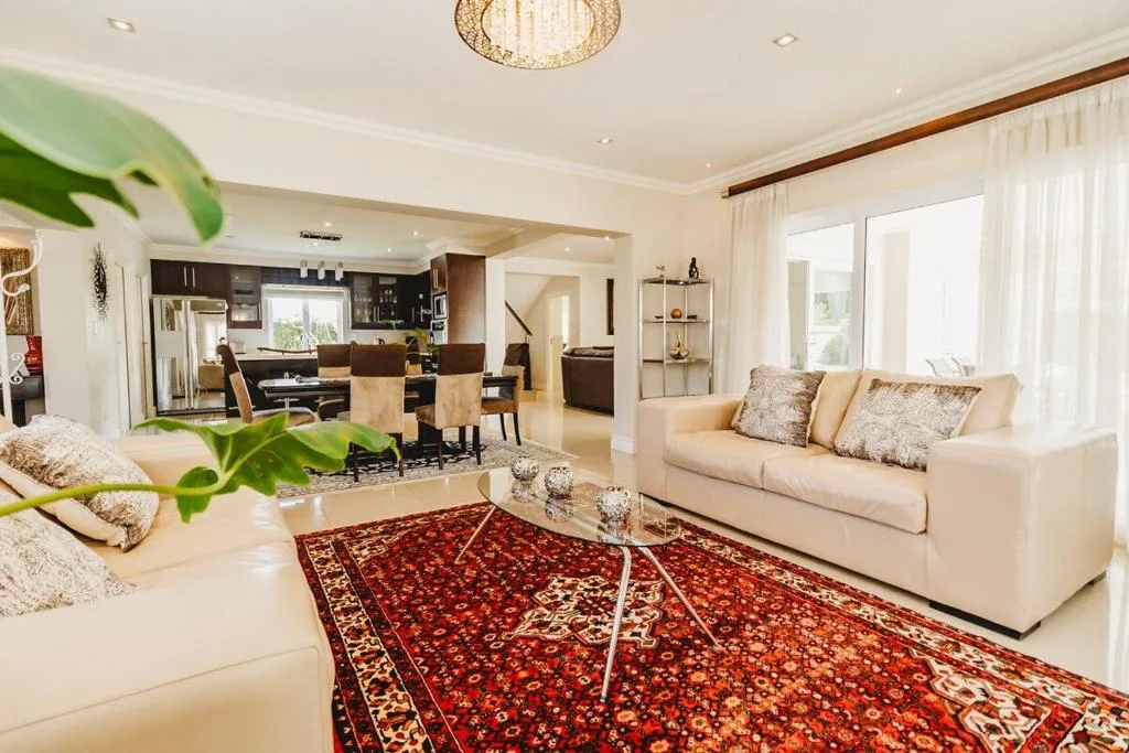 Spacious lounge with cream sofas, decorative red rug, and open-plan kitchen view