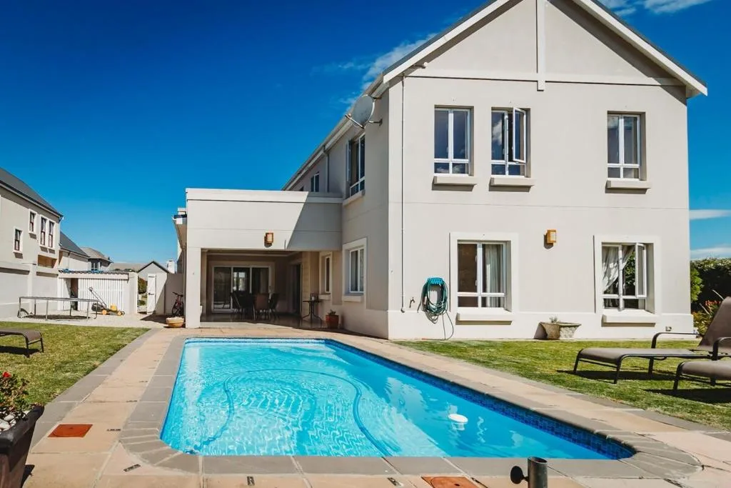 Swimming pool with modern white house and manicured garden backdrop