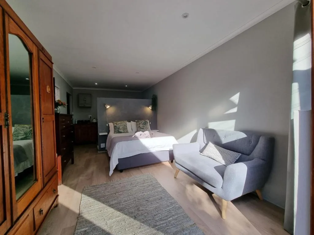 Bright bedroom with two beds, armchair, wooden wardrobe, and natural light