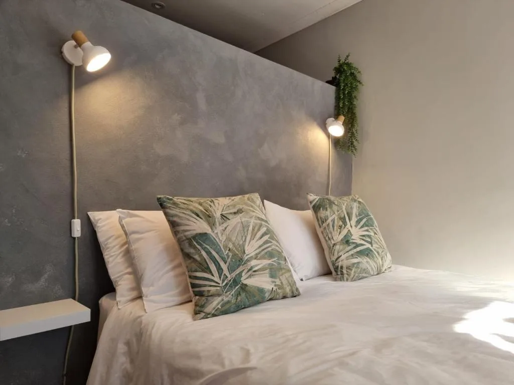 Modern bedroom with white bedding, botanical patterned pillows, and wall lighting