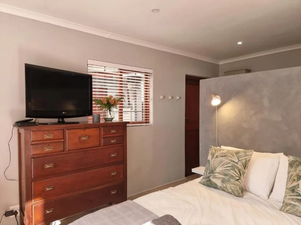 Bedroom with queen bed, wooden dresser, wall-mounted TV, and striped shutters