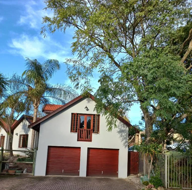 White cottage with red roof and garage doors, surrounded by mature trees