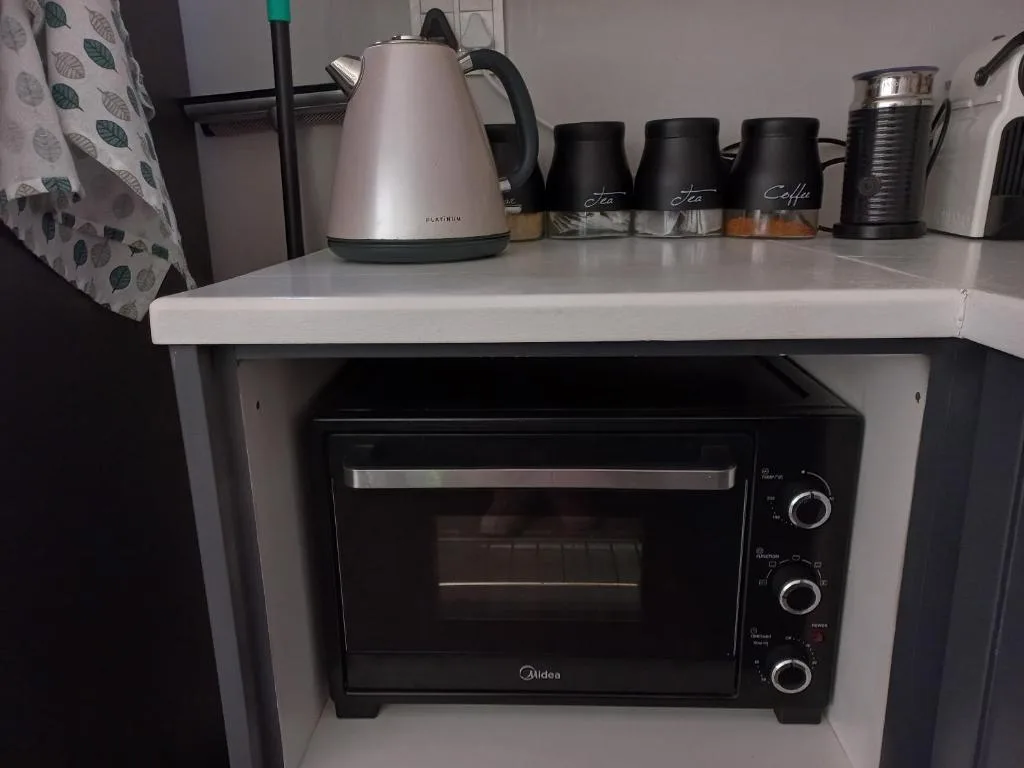 Compact kitchen corner with electric oven and kettle on white counter