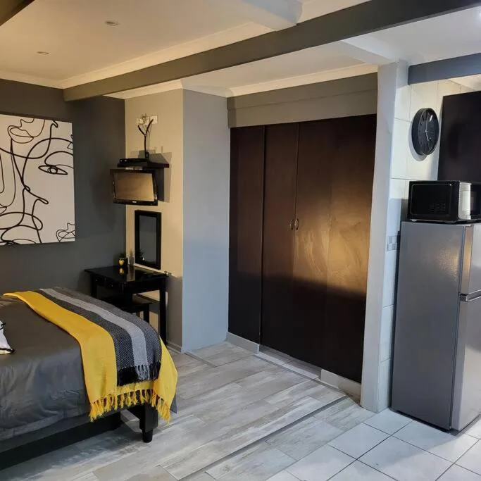 Modern bedroom with bed, dark wardrobe, and kitchenette visible in corner