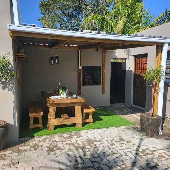 Covered patio with wooden dining table, benches, and artificial grass flooring