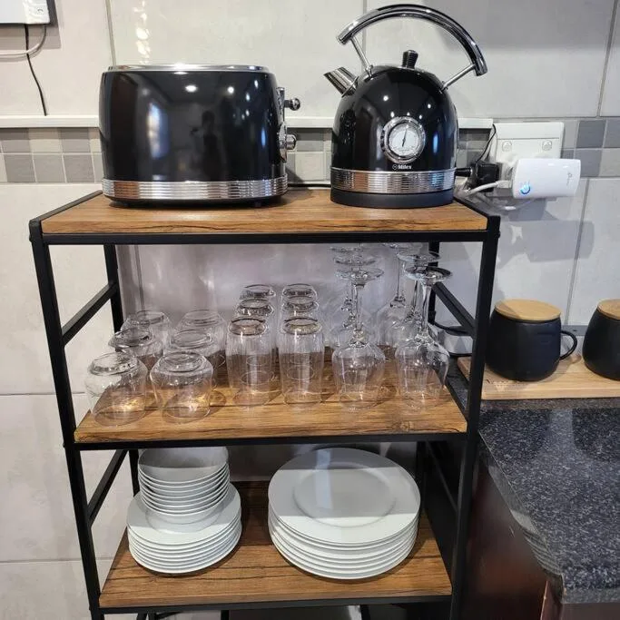 Black kettle and toaster on wooden shelf with glasses and dishes