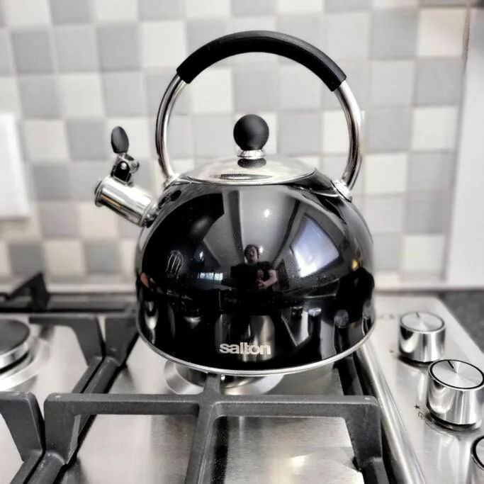 Black stainless steel kettle on kitchen stovetop with checkered backsplash