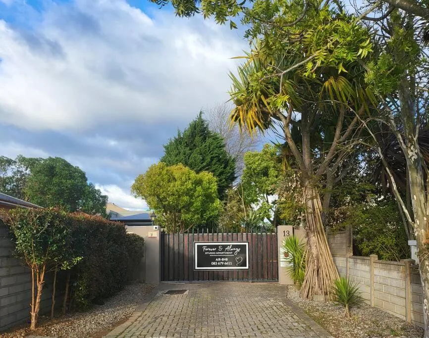 Gated entrance with driveway, palm tree, and manicured garden landscaping