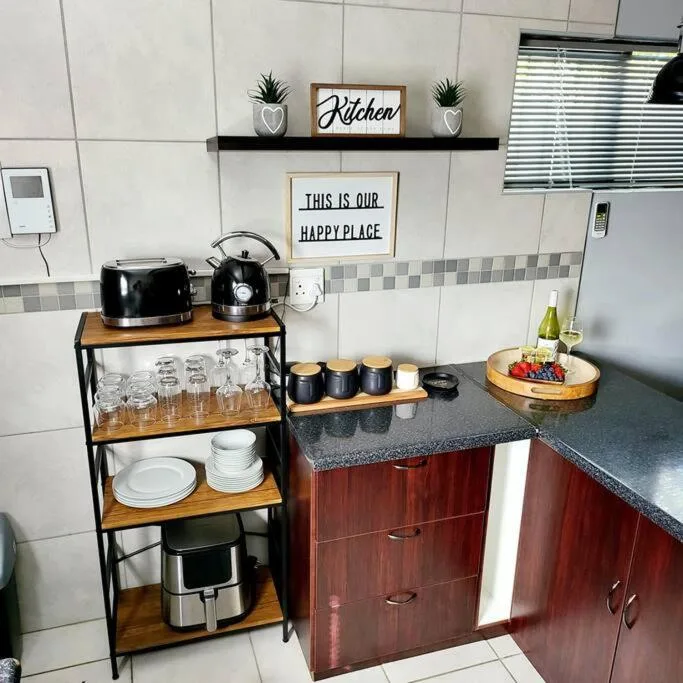 Compact kitchen with red cabinetry, black kettle and toaster, open shelving with glassware and decor