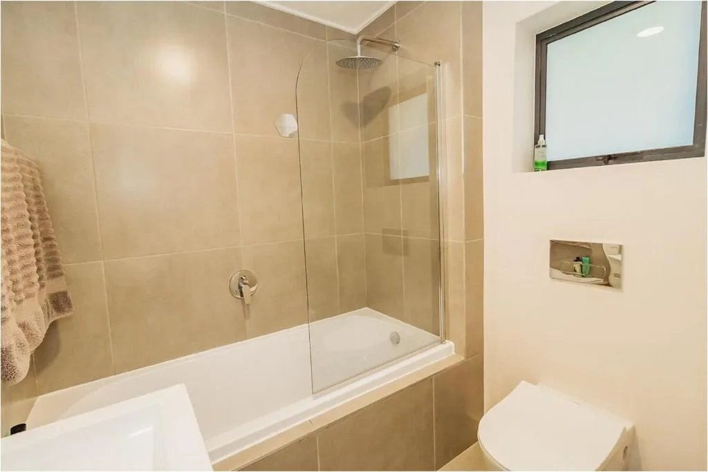 Modern bathroom with glass shower enclosure over bathtub and white toilet
