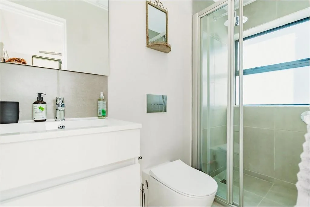 Modern bathroom with white vanity, toilet, and glass shower enclosure with blue trim