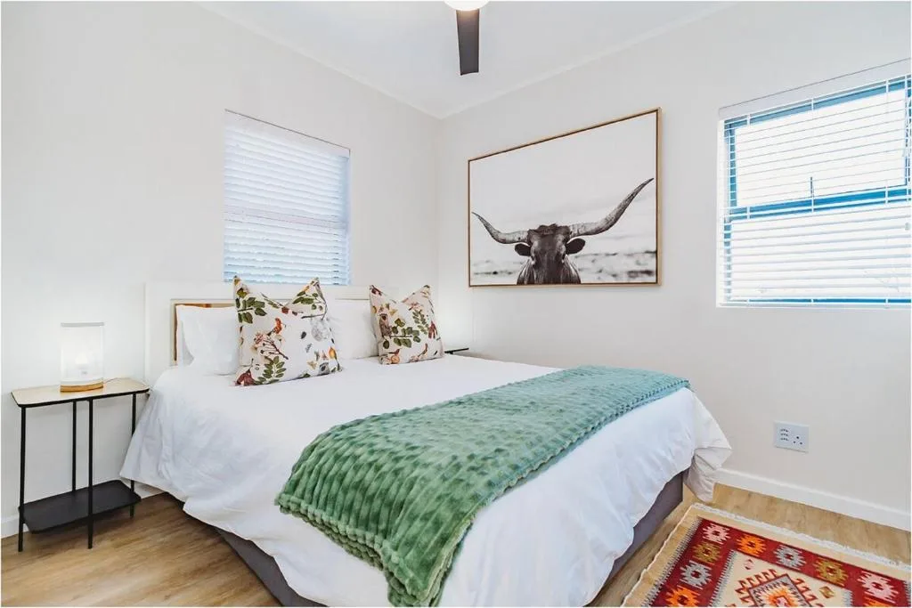 Bright bedroom with queen bed, floral pillows, green throw blanket, and wildlife art