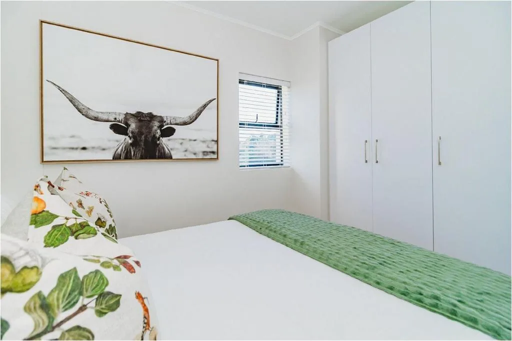 Bright bedroom with queen bed, white built-in wardrobes, and framed bull artwork