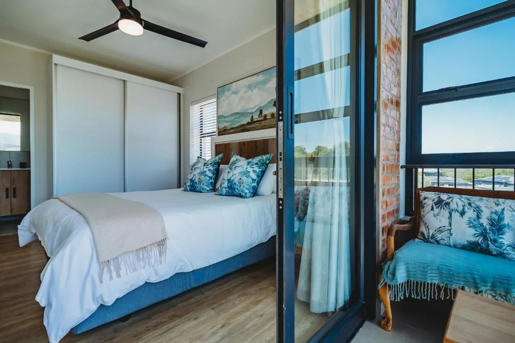 Modern bedroom with queen bed, blue pillows, ceiling fan, and scenic windows