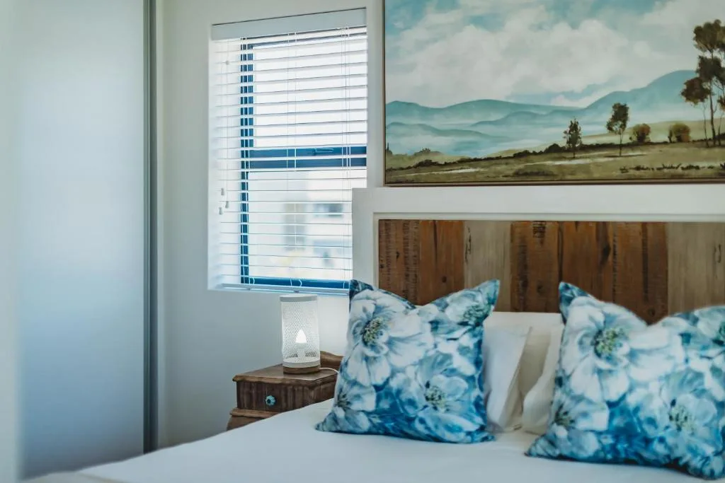 Bedroom with blue floral pillows, wooden headboard, and mountain artwork
