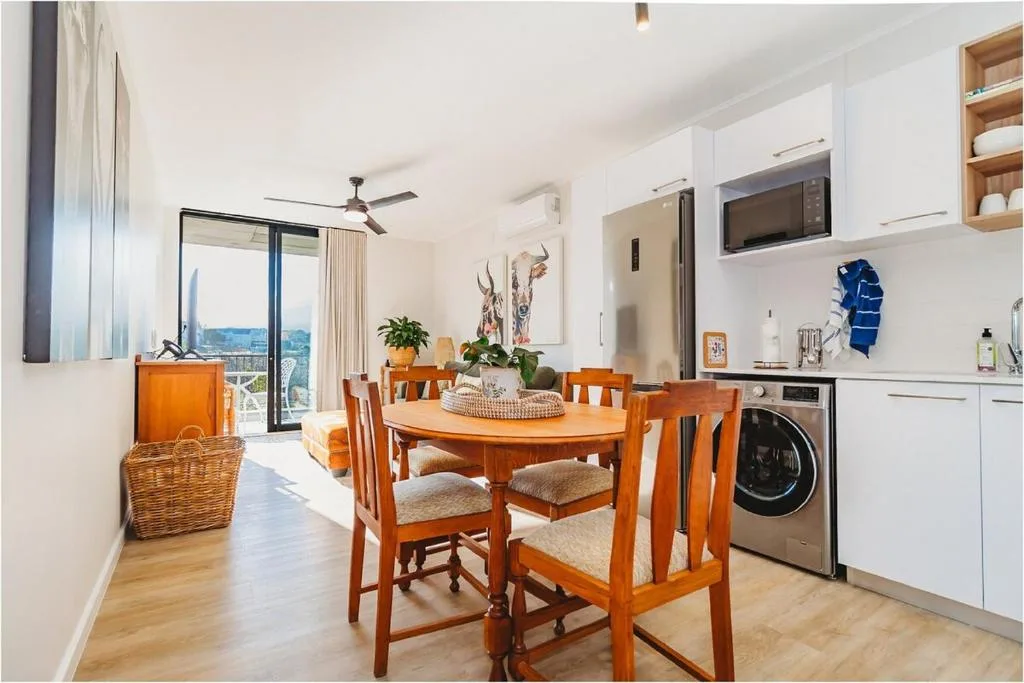 Modern dining area with wooden table, chairs, and kitchen visible in background