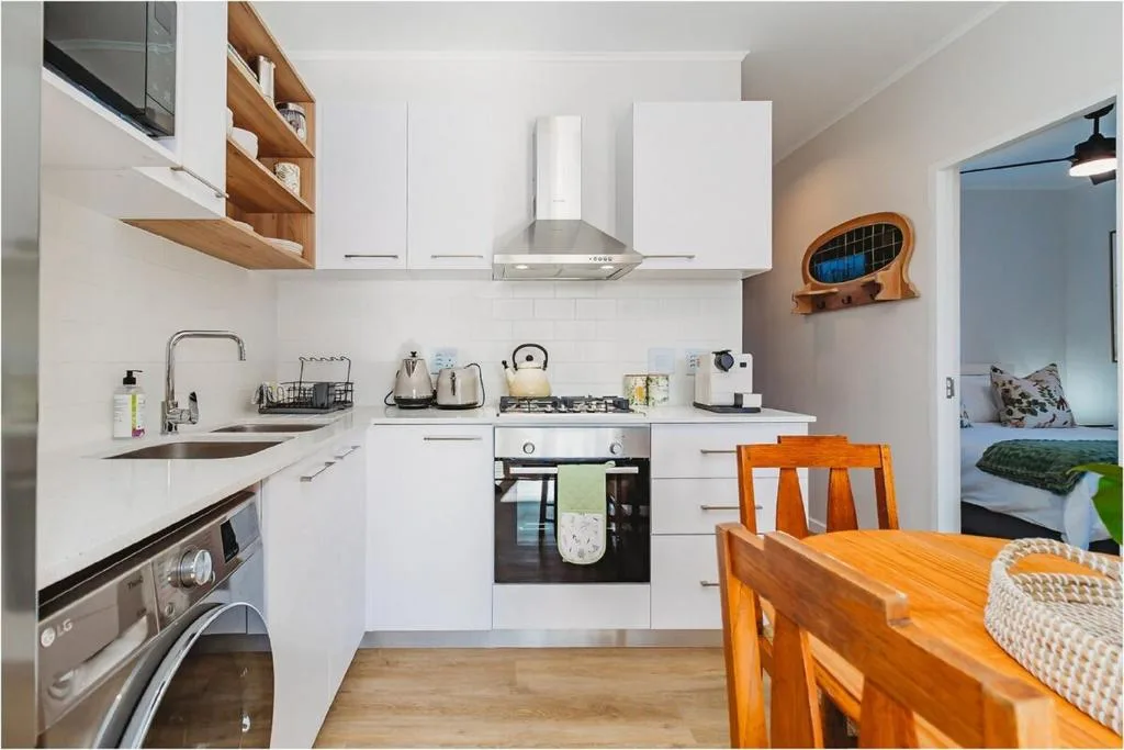 Modern white kitchen with stove, sink, and wooden dining table in foreground